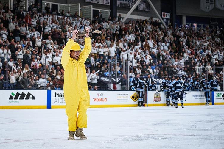 A man holds a fish over his head on the ice at a hockey game